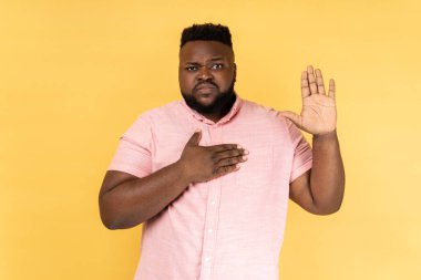 Ciddi vatansever bir adamın portresi pembe gömlekli, kalbinin üzerine el ele tutuşmuş, mahkemede, onurda ve vicdanında doğruyu söyleyeceğine yemin eden bir hukukçu. Sarı arka planda kapalı stüdyo çekimleri.