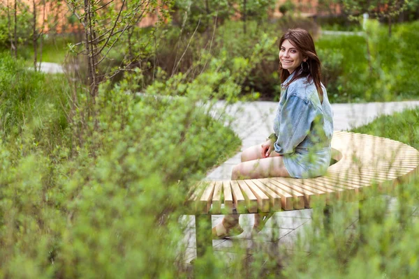 Yeşil Parktaki Ahşap Bankta Oturan Kot Ceketli Güzel Bir Kadının — Stok fotoğraf