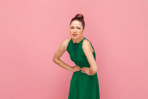 不满意的不健康女人的画像 手放在肚子上 痛苦不堪 穿着绿色衣服 在粉色背景下被隔离的室内拍摄 — 图库照片