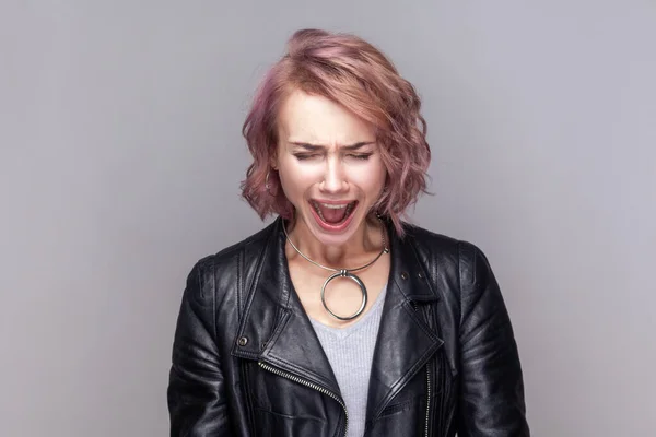 Portrait of despair sad depressed woman with short hairstyle standing screaming loud, having problems on her work, wearing black leather jacket. Indoor studio shot isolated on grey background.