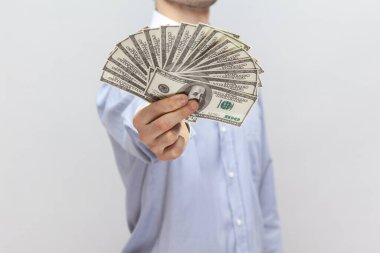 Bilinmeyen bir adamın portresi elinde dolar banknotlarının büyük bir hayranıyla ayakta duruyor, maaşını gösteriyor, açık mavi gömlek giyiyor. Gri arka planda izole edilmiş kapalı stüdyo görüntüleri.