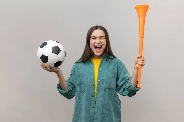 形象的兴奋女人拿着牛角和足球 快乐的尖叫 支持最喜爱的足球队 穿着休闲风格的夹克 在灰色背景下被隔离的室内拍摄 — 图库照片