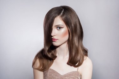 Kendine güveni tam esmer, güzel saç ve makyajlı esmer bir kadının esrarengiz bir ifadeyle kameraya bakan portresi. Gri arka planda izole edilmiş kapalı stüdyo görüntüleri.