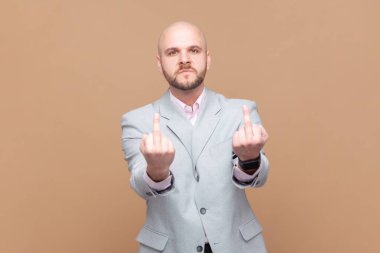 Orta parmak gösteren kızgın kel sakallı adamın portresi, kaba bir jest, nefret ve dargınlıkla dolu, gri ceket giyen. Kahverengi arka planda kapalı stüdyo çekimleri.