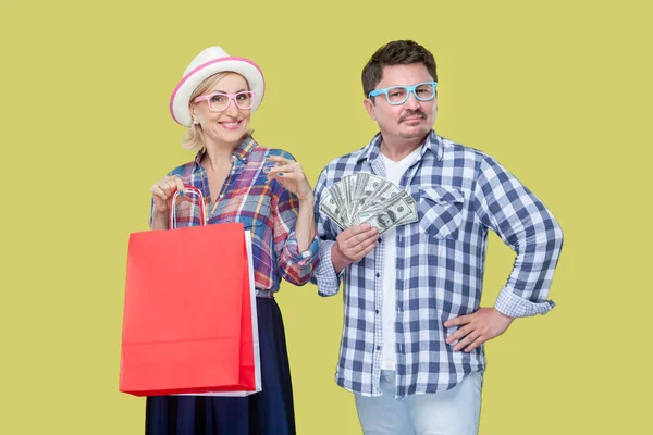 友人のカップル 大人の男女 カジュアルなチェッカーのシャツで一緒にショッピングバッグとドル紙幣のファン イエローバックで隔離された屋内スタジオショット — ストック写真