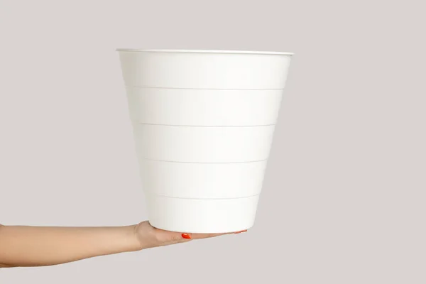 白いプラスチックのゴミ箱を示す女性の手のクローズアップ 灰色の背景で隔離された屋内スタジオショット — ストック写真