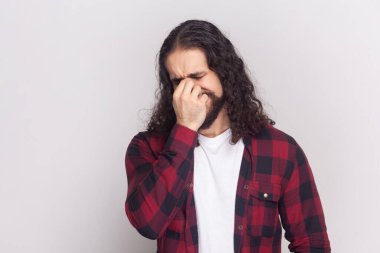 Kareli kırmızı tişörtlü, uzun kıvırcık saçlı, kederli, umutsuz adam karısı ya da kız arkadaşıyla tartıştıktan sonra depresyona giriyor. Stresli görünüyor. Gri arka planda izole edilmiş kapalı stüdyo görüntüleri.