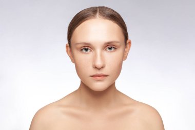 Çıplak omuzlarla kameraya bakan, mükemmel ciltli, çekici, ciddi bir kadının yakın plan portresi. Kapalı alanda çekilen çekim gri arka planda izole edildi.