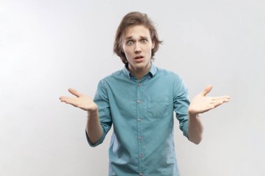 Mutsuz, stresli bir gencin portresi. Kollarını kaldırdı ve negatif duygularını ifade etti. Yüzü asık, mavi gömlek giyiyor. Gri arka planda izole edilmiş kapalı stüdyo görüntüleri.