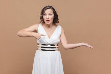 Şok olmuş orta yaşlı bir kadının portresi elini yana açıyor ve kapaktaki fotokopi alanını işaret ediyor, harika reklamlar yapıyor, beyaz elbiseler giyiyor. Açık kahverengi arka planda kapalı stüdyo çekimleri.