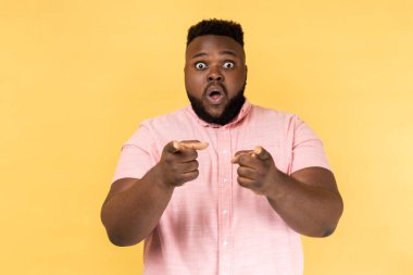 Hey sen! Pembe tişörtlü, ağzı açık, şok olmuş sakallı bir adamın portresi seni işaret ediyor, seçim yapıyor ve şaşkınlığını dile getiriyor. Sarı arka planda kapalı stüdyo çekimleri.