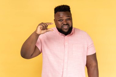 Çok küçük. Pembe gömlekli hayal kırıklığına uğramış bir adamın portresi biraz jest yapıyor ve kameraya sırıtıyor, boyunu ölçüyor, daha fazlasına ihtiyacı var. Sarı arka planda kapalı stüdyo çekimleri.