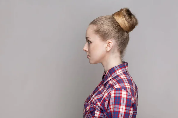 チェッカーのシャツを着た濃縮された表情で前方に立っている真面目な自信のある女性のサイドビューの肖像 灰色の背景で隔離された屋内スタジオショット — ストック写真