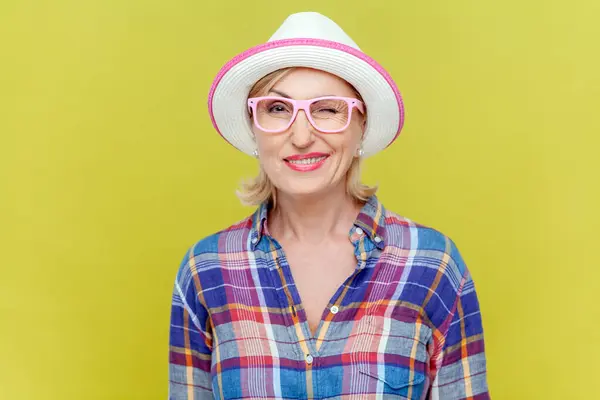 シャツ 眼鏡の陽気で遊び心のある成熟した女性は カメラ 反応で笑い ウィンクしています 黄色の背景に隔離された屋内スタジオショット — ストック写真