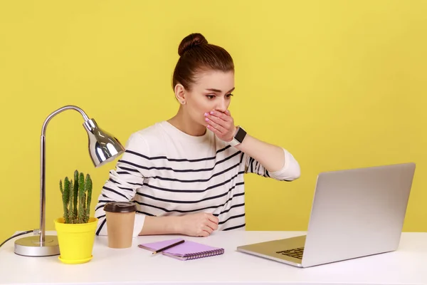 portrait of shocked woman office worker covering mouth, looking at laptop screen with terrified expression, found scary secret. Indoor studio studio shot isolated on yellow background.