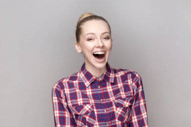Neşeli, neşeli, son derece mutlu bir kadının portresi. Saç stili, güzel şakalar duyan, yüksek sesle gülen, kareli gömlek giyen. Gri arka planda izole edilmiş kapalı stüdyo görüntüleri.