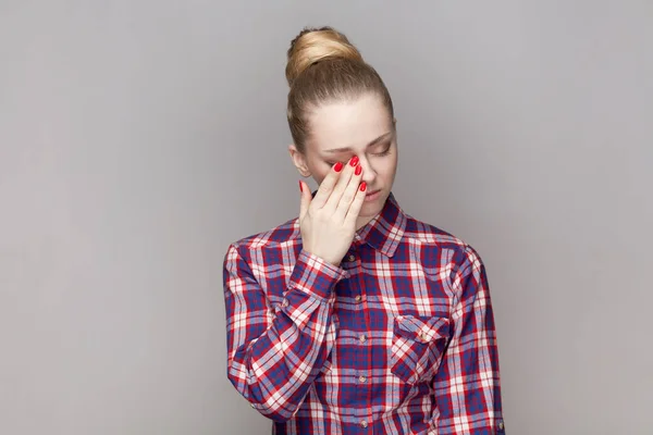 Portrait of despair sad stressed woman with bun hairstyle crying, having problems, wiping her tears, being in depression, wearing checkered shirt. Indoor studio shot isolated on gray background.