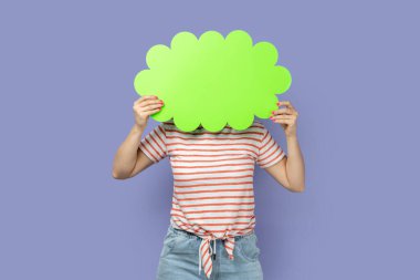 İsimsiz sarışın kadının portresi çizgili tişört giymiş yüzünü yeşil baloncuğun arkasına gizliyor mesaj için, terfi için fotokopi alanı. Mor arka planda izole edilmiş kapalı stüdyo çekimi.