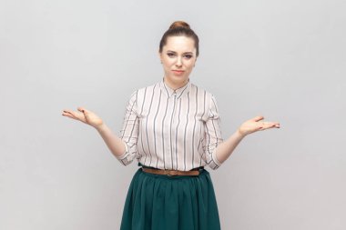 Bunu nasıl yaparsın? Çizgili gömlek ve yeşil etek giyen, strese girmiş, gergin bir kadın portresi rahatsız edici bir görünüm sergiliyor. Gri arka planda izole edilmiş kapalı stüdyo görüntüleri.