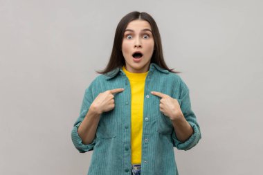 Vay canına, ben en iyisiyim. Koyu renk saçlı kadının kendini göstermesi ve şaşkınlıkla bakması, başarıdan gurur duyması, günlük tarz ceket giymesi. Gri arka planda izole edilmiş kapalı stüdyo görüntüleri.