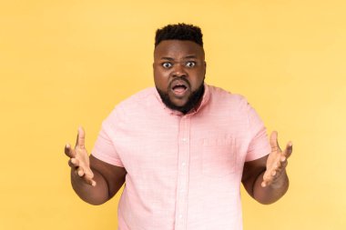 Pembe tişört giyen, ne istediğini soran ve el sallayan sinirli bir adamın portresi. Aile kavgası, yanlış anlaşılma. Sarı arka planda kapalı stüdyo çekimleri.