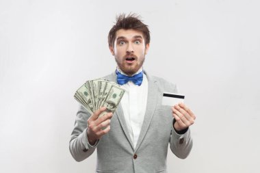 Elinde dolar banknotları ve kredi kartı bulunan, gri takım elbiseli ve mavi papyonlu, şaşırtıcı sakallı adamın portresi. Gri arka planda izole edilmiş kapalı stüdyo görüntüleri.