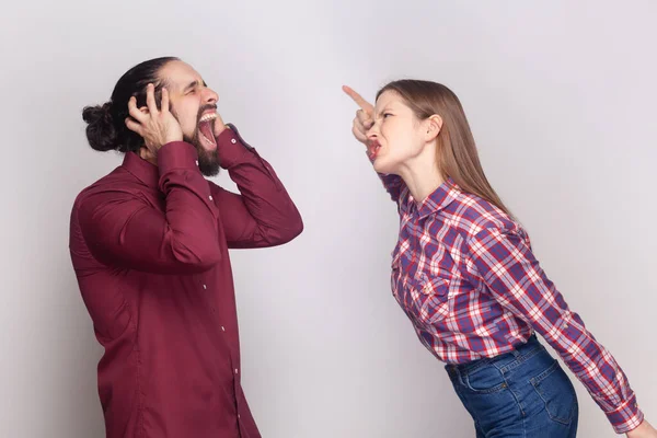 一个脾气暴躁的女人和一个恼怒的男人站在一起 妻子尖叫着指着他的丈夫 男人捂着耳朵 在灰色背景下被隔离的室内拍摄 — 图库照片