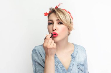 Çekici, çekici, sarışın, mavi kot gömlek giyen ve kırmızı ruj süren kırmızı saç bandı takan güzel bir kadının portresi. Gri arka planda izole edilmiş kapalı stüdyo görüntüleri.