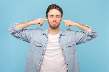 Bu korkunç sesi çıkarmayı kes. Stresli adam çaresizlik, gözleri kapama, kulakları parmaklarla tıkama, yüksek ses ve müzikten rahatsız olma. Mavi arkaplanda kapalı çekim.