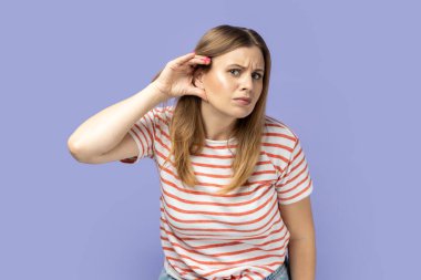 Seni duyamadım. Dikkat çeken, çizgili tişörtlü, kulak dibinde el ele tutuşan, sessiz konuşmaları dinlemeye çalışan, dedikoduları duyan sarışın kadının portresi. Mor arka planda izole edilmiş kapalı stüdyo çekimi.