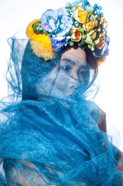 Çiçekli şapkası ve mavi duvağı olan, yüzünü gizleyen, başka tarafa bakan şehvetli, gizemli, güzel bir mankenin yan görünümü. Gri arka planda izole edilmiş kapalı stüdyo görüntüleri.