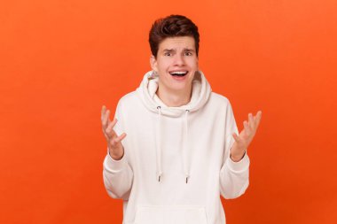 Hayal kırıklığına uğramış beyaz kapüşonlu genç bir adamın portresi şok ve yanlış anlaşılmayla el sıkışıyor. Nasıl imzalayabilirsin ki? Turuncu arka planda kapalı stüdyo çekimleri.