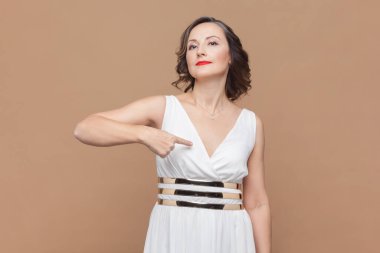 Üstesinden gelebilirim. Kararlı kadın kendini işaret eder, gururlanır ve kendi başarılarıyla övünür, beyaz elbise giyerek kendi yardımını teklif eder. Açık kahverengi arka planda kapalı stüdyo çekimleri.