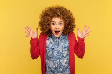 Portrait of emotive woman with Afro hairstyle raises hands and has happy face expression feels excited, being full of happiness. Indoor studio shot isolated on yellow background. clipart