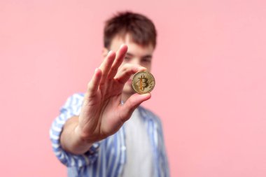 Gömlek giyen çekici esmer bir gencin portresi altın bitcoin kripto para birimi kârı sağlıyor. Pembe arka planda kapalı stüdyo çekimleri.