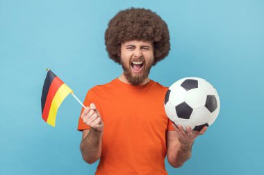 Afro saç stili, Alman bayrağı taşıyan deli bir adamın portresi ve futbol siyah beyaz klasik topu ve maç izleyip tezahürat yapıyor. Mavi arka planda kapalı stüdyo çekimi.