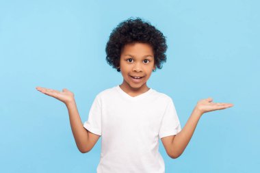 Neşeli, neşeli, pozitif, kıvırcık saçlı küçük bir çocuğun portresi. Avuç içi reklam alanındaki fotokopi alanını sunuyor. Mavi arka planda kapalı stüdyo çekimi.