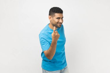 Gülümseyen mutlu, traşsız, mavi tişörtlü, parmağını gösteren, buraya gelip kameraya bakan adamın portresi. Gri arka planda izole edilmiş kapalı stüdyo görüntüleri.