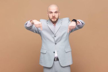 Burada ve şimdi. Kel adam küstahça aşağı bakıyor, derhal itaat talep ediyor, otoritesini gösteriyor, gri ceket giyiyor. Kahverengi arka planda kapalı stüdyo çekimleri.