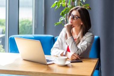 Laptop üzerinde çalışan düşünceli bir kadının portresi yeni bir proje düşünüyor çenesini tutuyor karar veriyor, ceket giyiyor ve tişört giyiyor. Kapalı çekim, kafe ya da ofis geçmişi.