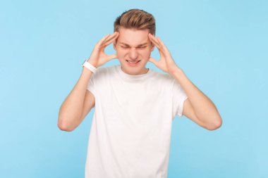 Beyaz tişört giyen hasta bir adamın portresi. Acı veren tapınaklara masaj yapıyor, korkunç baş ağrısı çekiyor, suratını asıyor. Mavi arka planda kapalı stüdyo çekimi