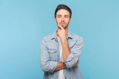 Tüylü, çenesi kıllı ve düşünceli bir portre, planlar yapar, yeni projeler düşünür, kot gömlek giyer. Mavi arkaplanda kapalı çekim.