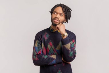 Düşünceli, Afro-Amerikan bir adamın portresi. Rastalı ve sakallı. İşini düşünüyor, çenesini tutuyor, yan bakıyor. Gri arka planda izole edilmiş kapalı stüdyo görüntüleri.