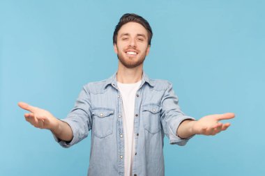 Kollarıma gel. Tıraşsız bir adamın, kameraya uzanan portresi, sana sarılmak için kollarını uzatan, dişlek tebessümle kameraya bakan, kot gömlek giyen. Mavi arkaplanda kapalı çekim.