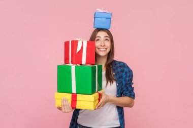 Gülümseyen neşeli kahverengi saçlı kadının portresi elinde hediyeler, başında hediyeler, bayramı kutlayan, kareli gömlek giyen. Pembe arka planda kapalı stüdyo çekimleri.