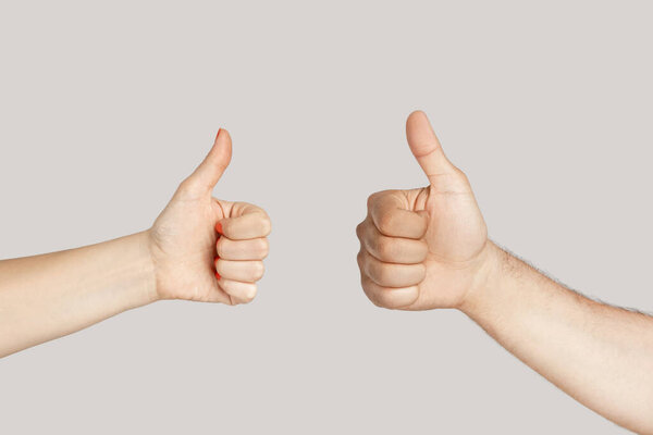 Closeup of diverse man and woman hands showing thumb up, like gesture, approved sign. Indoor studio shot isolated on gray background.