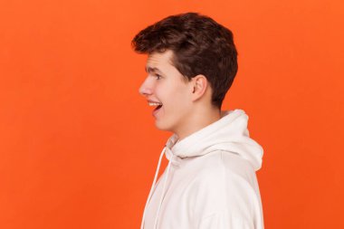 Beyaz kapüşonlu, ağzı açık kameraya bakan ve habere hoş bir şekilde şaşıran genç ve yakışıklı bir adamın yan görüntüsü. Turuncu arka planda kapalı stüdyo çekimleri.