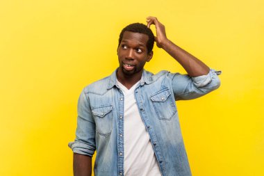 Düşünceli, düşünceli bir adamın portresi. Başını ovuşturuyor. Kafa karışıklığıyla bakıyor. Sarı arka planda kapalı stüdyo çekimleri.