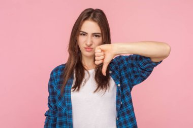 Hoşnutsuz kahverengi saçlı kadının portresi. Yüzü somurtkan, jest hatası gösteren, kareli gömlek giyen. Pembe arka planda kapalı stüdyo çekimleri.