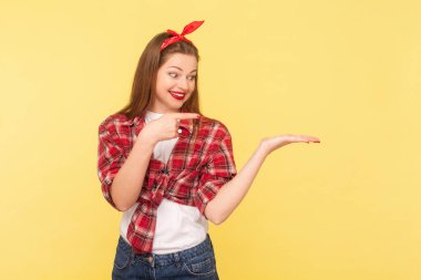 Kırmızı dudaklı hoş bir kadın avucunda boş bir yer sunuyor. Model, reklam alanı, kareli gömlek ve saç bandı takıyor. Sarı arka planda kapalı stüdyo çekimleri.